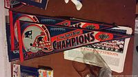 Two New England Patriots championship felt pennants on table with newspapers and collectibles around