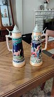 Front view of both steins showing relief scenes and lids