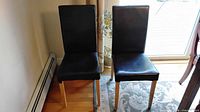 Front view of two black faux leather dining chairs with light wood legs