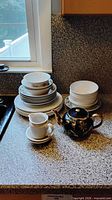Stack of plates and bowls, teapot, creamer with saucer on countertop
