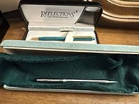 Both pens in respective cases; Reflections box open showing teal pen, Cross pen below in green felt case