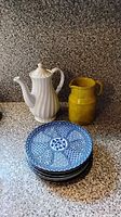 Stack of six patterned plates, white teapot, yellow pitcher