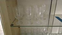Seven of eight clear etched goblets on glass shelf