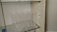 Eight clear glass Collins glasses on shelf