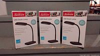 Front view of three boxed Sunbeam LED desk lamps
