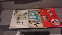 Close-up of three vintage sports programs detailing cover art and team matchups