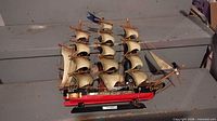 Front port-side view of full model ship with red hull, beige sails, anchor and stand visible.
