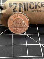 Beaver reverse of 1964 Canada 5-cent coin leaning on original paper roll