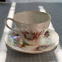 Side view of teacup on saucer showing form, floral design and gold trim