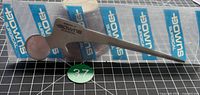 Front view of hip prosthesis letter opener sealed in sleeve with Downs Surgical branding visible