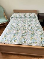 Overall view of bed frame with floral comforter, partial nightstand and chair visible