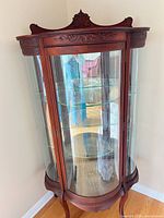 Full frontal angled view of curved glass curio cabinet showing door, shelves, legs