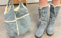 Boots on model’s feet next to matching tote showing color, height, and shearling trim