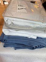 Stack showing packaged duvet cover, off-white linen, blue tablecloth