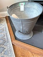 Front view of galvanized ash bucket showing pedestal and side handle