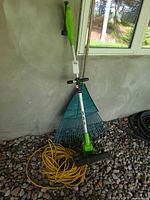 Trimmer, rake and extension cord leaning against wall