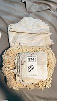 Stack of folded white linens and crocheted mats with auction tag visible