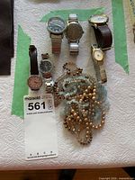 Group shot of six wristwatches and multiple beaded necklaces on table