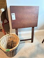 Gray wicker basket next to folding wooden TV tray table