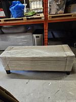 Full view of upholstered bench wrapped in plastic, showing front and legs