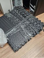 Stack of black diamond-tread EVA foam tiles with interlocking edges, wrapped in plastic
