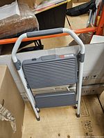 Front view of folded 2-step stool showing frame, steps, and handle