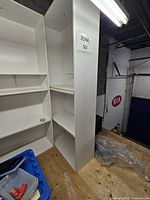 Full view of white tall shelving wardrobe unit on plywood floor