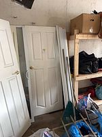 Door standing upright showing six-panel design, brass knob, white pull handle, and overall condition