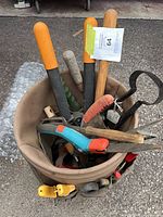 Front view of tan canvas bucket filled with assorted long-handled garden tools and pruning shears