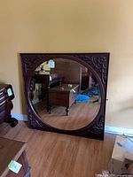 Full view of square carved mahogany frame mirror leaning against wall