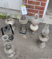 Group shot showing six oil and kerosene lamps with chimneys and one black lantern