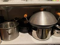 Shelf with stainless stockpot, sauté-wok on pot, additional small pots