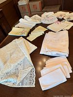 Overview of assorted folded linens including lace tablecloth, napkins and doilies on table