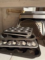 Stacked muffin tins, perforated pizza tray and cookie sheet visible
