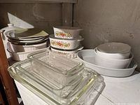 Stacked clear glass baking dishes and loaf pan in front of white bowls and metal trays