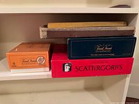 Shelf view showing orange Trivial Pursuit box, navy Trivial Pursuit box, red Scattergories box, additional stacked game components