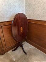 Side table shown folded upright against wall displaying oval top with inlaid medallion