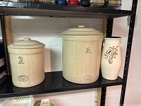 Side view of two Medalta crocks (2- and 5-Imperial) with lids and stoneware vase on shelf
