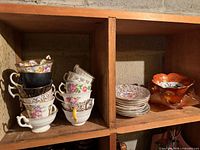Stacked assorted floral teacups, chintz saucers and two bowls in shelf cubbies