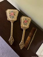 Front view of mirror back, brush back, and comb showing tapestry design and ornate frames