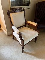 Front angled view of carved Victorian armchair showing upholstery and casters
