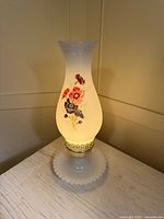 Lamp illuminated showing milk glass chimney, floral decal, brass trim on base
