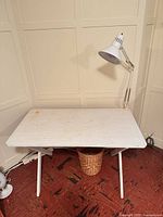 Front view of white drafting table with lamp and basket