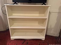 Front view of white painted wood bookcase with three shelves