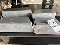 Four silver/grey Panasonic satellite speakers on glass shelf