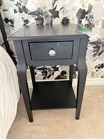 Full view of black wood nightstand beside bed