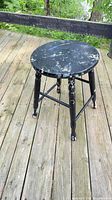 Full view of black paint-splattered wooden stool on deck