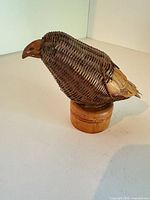 Left side view of wicker and wood bird on wooden pedestal