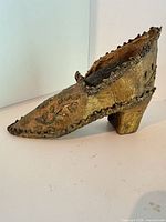 Left side view of gold and green paper mache shoe showing floral motif and heel