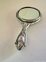 Front view of silver-plated hand mirror showing handle and glass
